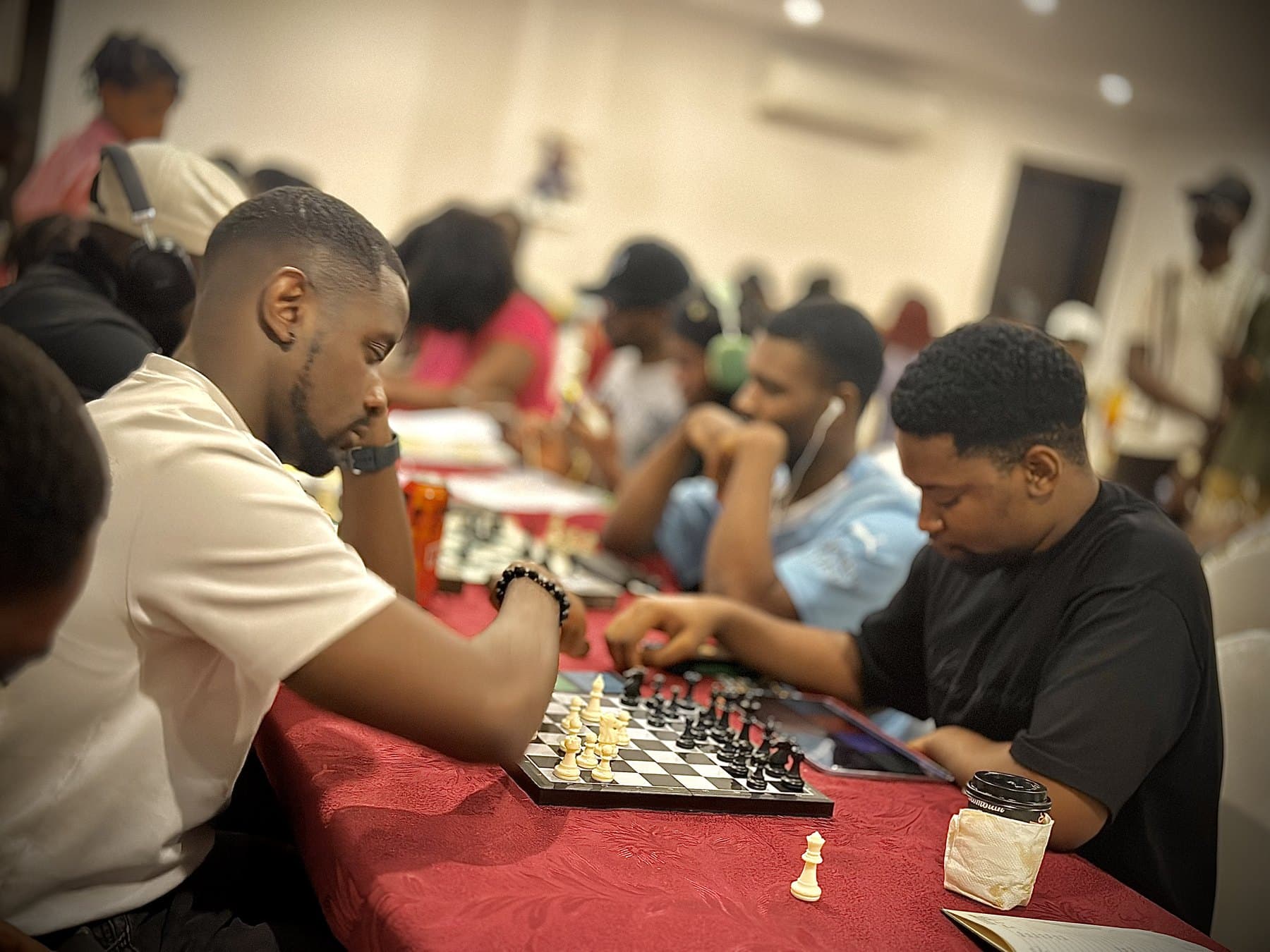 A row of players at tournament boards in a hall, several games under way at once.