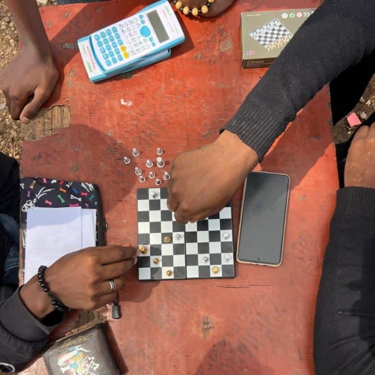 Seen from above: two players' hands either side of a board, with a clock, scoresheets and phones on the table.